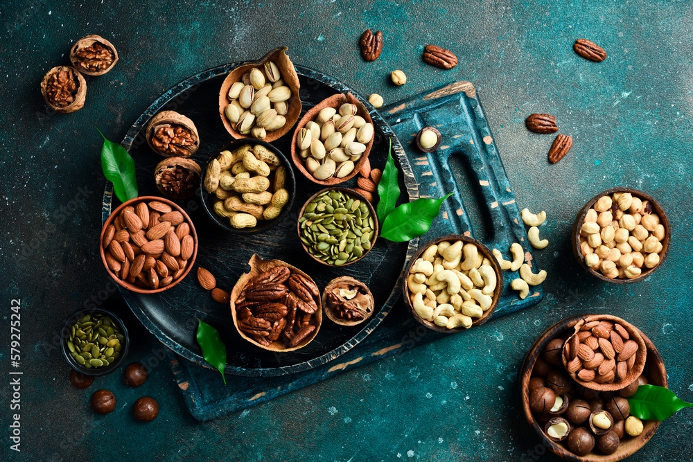 Peanuts, walnuts, almonds, hazelnuts and cashews mixed together in wooden bowls. Top view. On a dark background. Peanuts, walnuts, almonds, hazelnuts and cashews mixed together in wooden bowls. Top view. On a dark background.