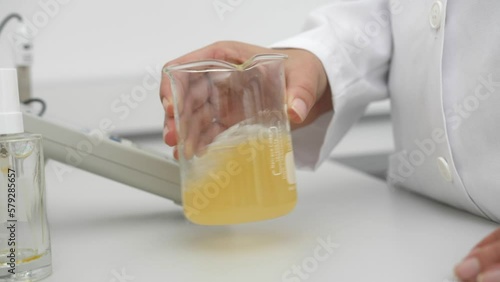 closeup of female scientist mixing yellow liquid in beaker in scientific lab slow motion