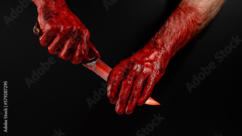 A man wipes a bloody knife with his hand on a black background. 