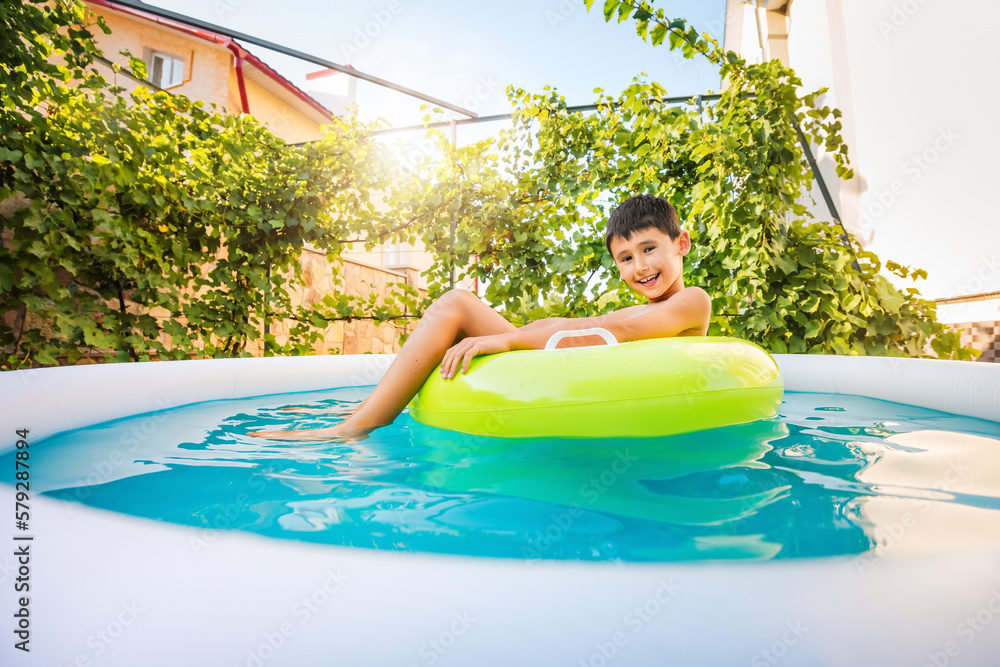 Little boy swims in an inflatable circle in home pool near the house. Wonderful sunlight greenery grape background. Wide angle shooting.