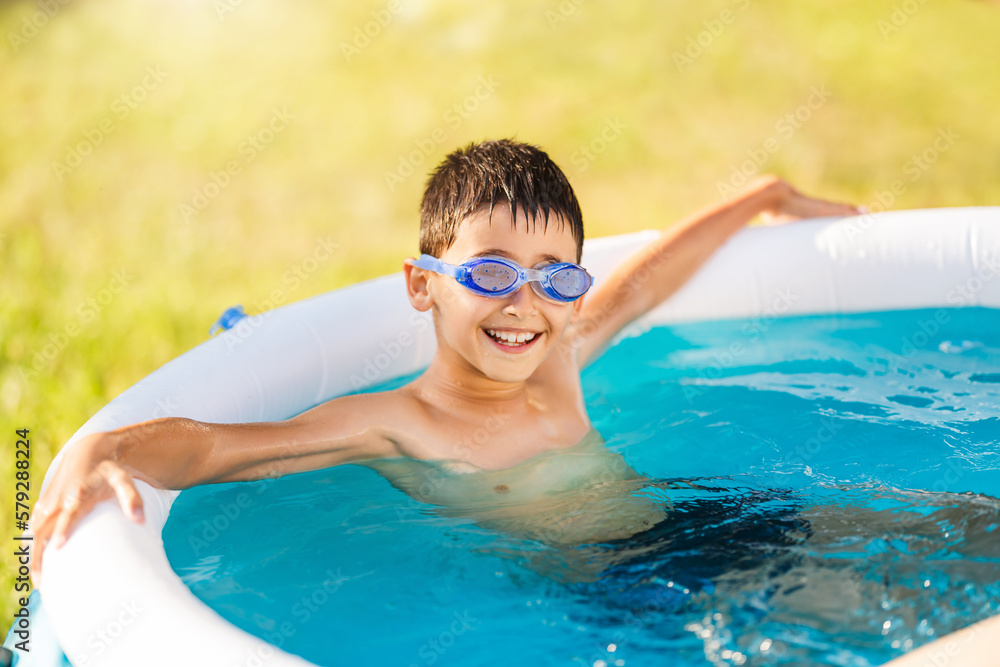 Happy child resting in inflatable round pool at home outdoors.
