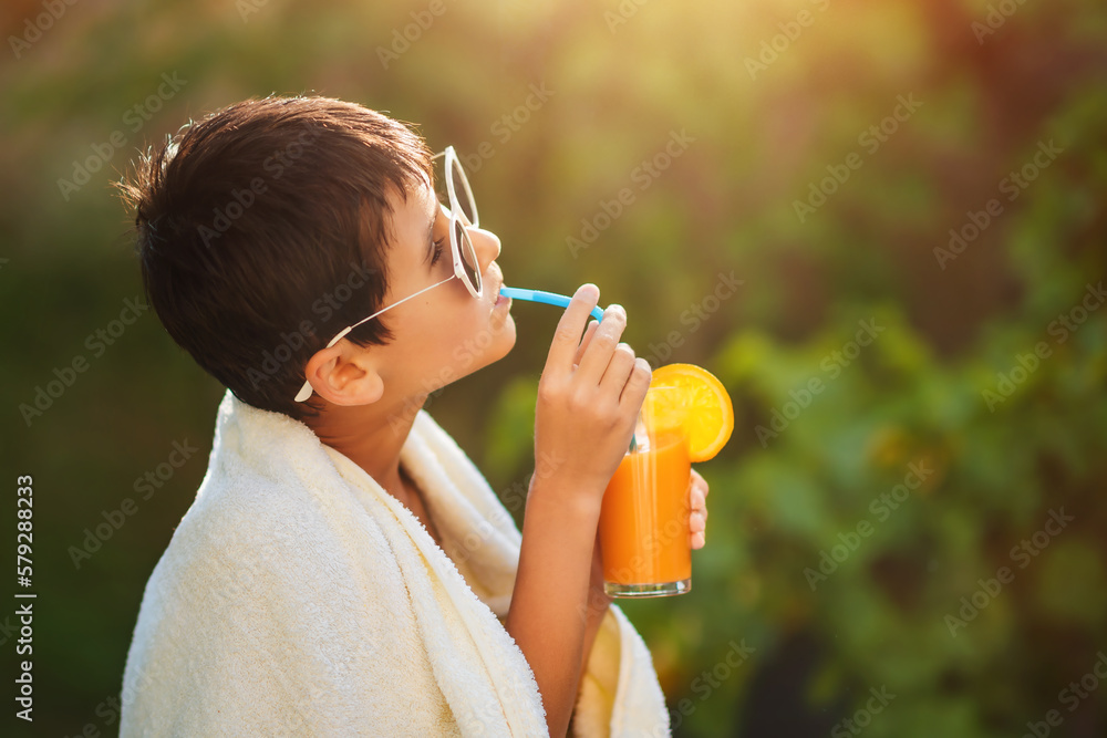 Child drinks orange juice through a straw from a glass, outdoor.