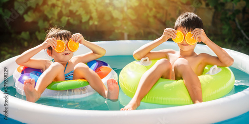 Children relax in the inflatable round pool in backyard. Kids play with orange slices.