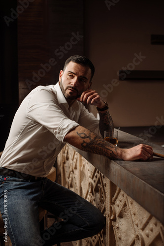 Handsome bearded male in shirt and jeans with glass of whiskey and cigar in the bar or pub © rostyslav84