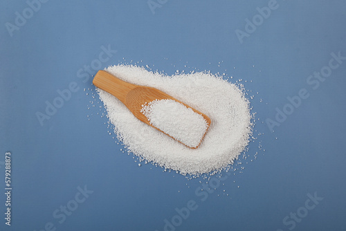 Pile of White crystalline chemical powder and wooden scoop. Sodium benzoate, sodium salt of benzoic acid on blue. Food additive E211 used as preservative in medicines and cosmetics photo