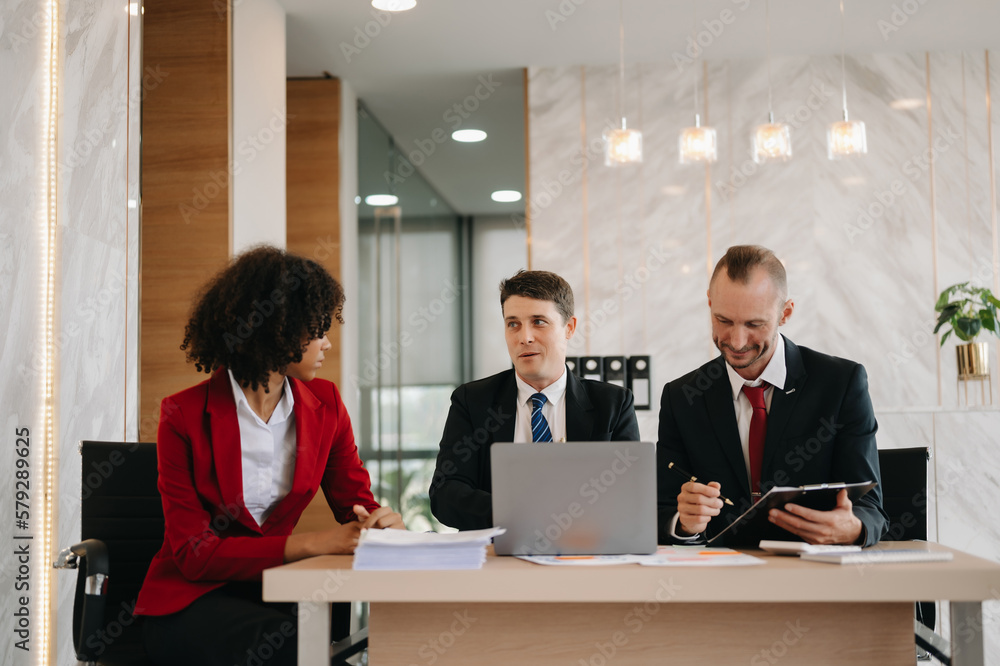 Happy businesspeople while collaborating on a new project in an office. Group of diverse businesspeople using a laptop and tablet in office.. Happy businesspeople while collaborating on a new project in an office. Group of diverse businesspeople using a laptop and tablet in office..