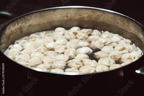 Small size meat dumplings are boiling in a pot on the stove. Pelmeni are the traditional national Russian cuisine. Italian ravioli. Food for children. Dish for kid. Cooking lunch or dinner for family