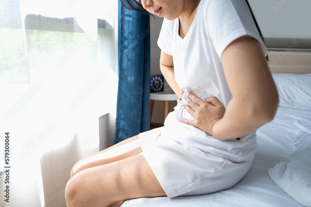 Obraz premium Woman having stomachache on bed in bedroom. Menstrual pain or gastrointestinal disease concept.