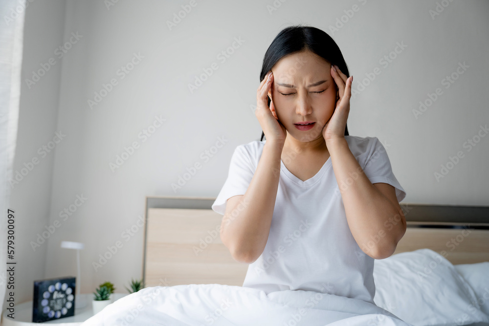 Asian woman having headache maybe migraine in the morning in bed. She is massaging her temples. Asian woman having headache maybe migraine in the morning in bed. She is massaging her temples.