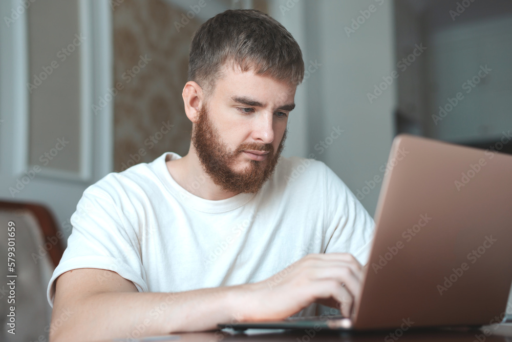 Young bearded concentrated man use laptop computer at home in living room with serious face, typing on keyword Young bearded concentrated man use laptop computer at home in living room with serious face, typing on keyword