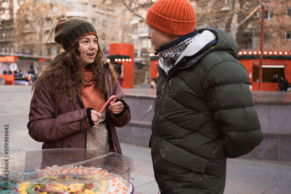 Adult couple in love bying christmas sweets at candy bar in street market at winter holidays