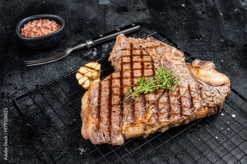 Grilled T-bone or Porterhouse beef meat Steak on a rack. Black background. Top view