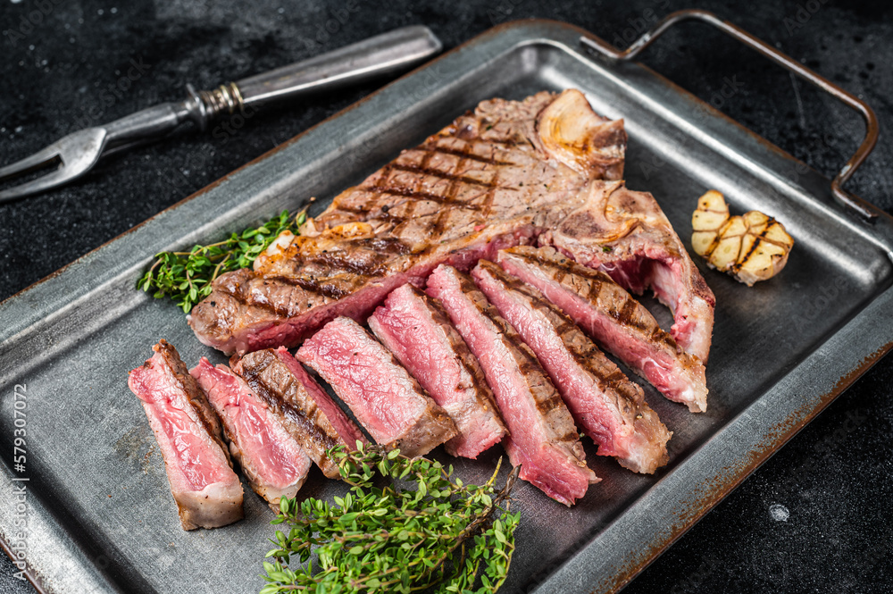 Medium rare Grilled T-Bone Steak,  Florentine steak  sliced in a steel tray. Black background. Top view