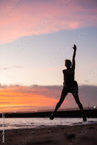 A young girl admires the sunset on the ocean  enjoys life  arms outstretched to the sides  rear view.
