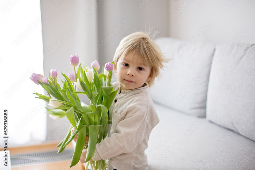 Beautiful blond boy, giving mother flowers and box with little gift for mothers day Beautiful blond boy, giving mother flowers and box with little gift for mothers day
