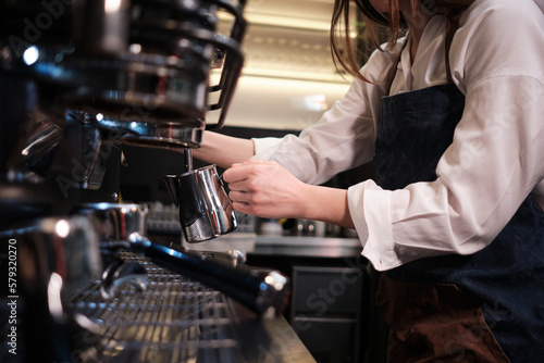 Close up of a barista preparing milk for coffee on a espresso machine in coffee shop.