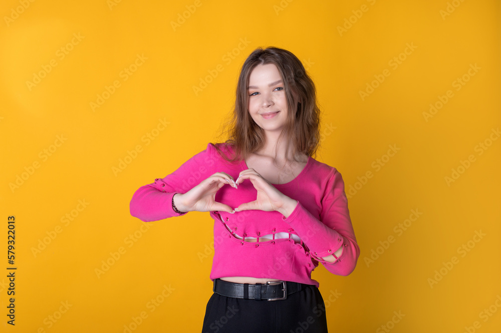 Photo of a young cute girl showing a heart shape, wearing a pink sweater on a yellow background Photo of a young cute girl showing a heart shape, wearing a pink sweater on a yellow background
