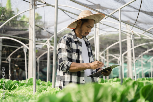 Asian farmer using hand holding tablet and organic vegetables hydroponic in greenhouse plantation. hydroponic salad vegetable garden owner working.