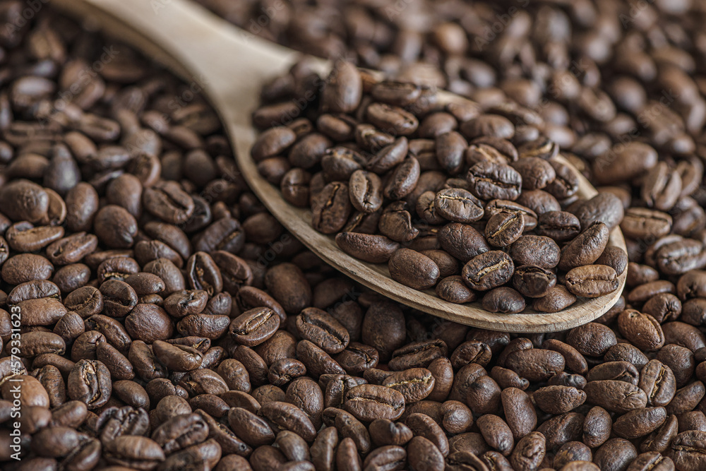 Fototapeta premium coffee background of roasted coffee beans on a wooden spoon close up, shallow depth of field