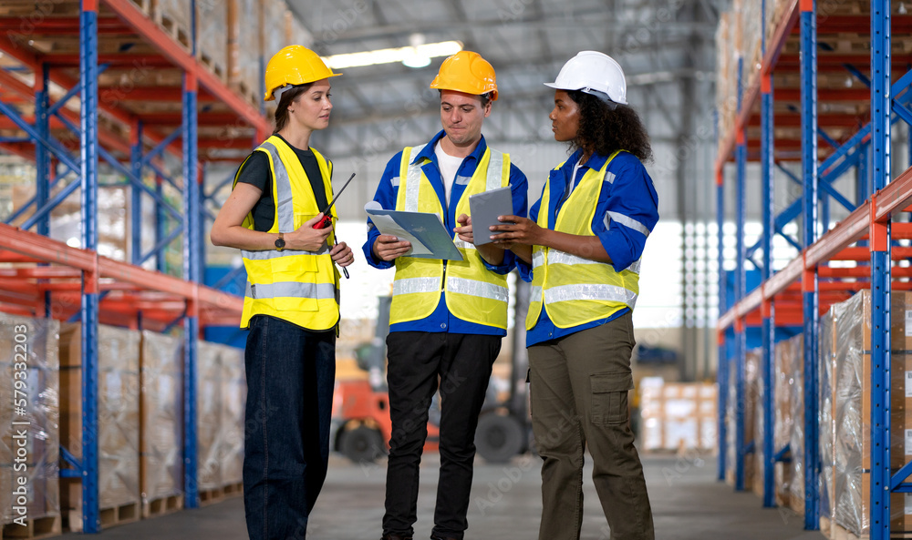 Multiracial group of warehouse workers working at storage room in factory. Multiethnic woman worker and colleague talking inventory discussion in distribution warehouse. Diverse people work together Multiracial group of warehouse workers working at storage room in factory. Multiethnic woman worker and colleague talking inventory discussion in distribution warehouse. Diverse people work together