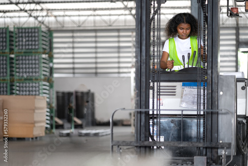 Multiracial female warehouse worker driving forklift truck in distribution storehouse. Woman vehicle driver working in shipping storage factory lifting, moving and unloading cargo ready for delivery.