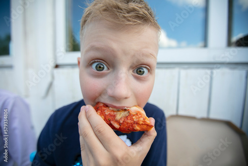 Billede på lærred Photo Wide-angle lens of a little boy who eats pizza with his eyes wide open