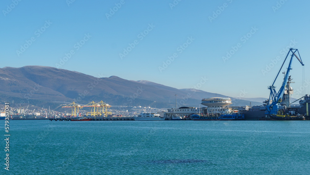 View of Novorossiysk Commercial Sea Port to container ships, Port cranes. Turquoise water in foreground. Largest Russian port in Tsemes bay of the Black Sea. Novorossiysk, Russia - December 20, 2022