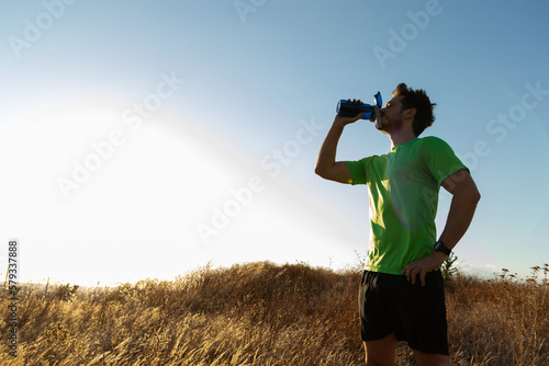 Fotografía Athlete man hydrates after running in nature at sunset