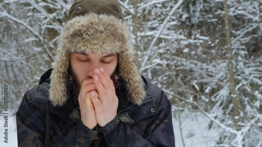 Man froze on walk outside in winter and trying to warm up, warming hands with breath. Concept of problem and peculiarities nature of North. Guy in hat with earflaps in snow park. Man froze on walk outside in winter and trying to warm up, warming hands with breath. Concept of problem and peculiarities nature of North. Guy in hat with earflaps in snow park.