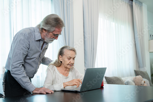 Retired old Asian male and his wife hand use Asian senior couple working and check data information with laptop on table in living room at home.