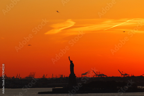 Silhouette of Statue of Liberty and Liberty Island in New York against an orange sunset sky