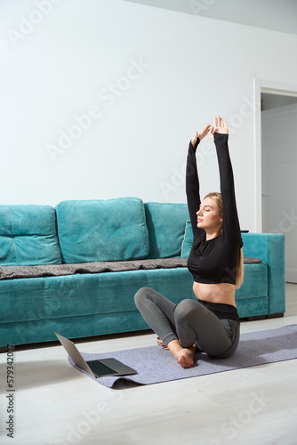 Calm female doing yoga on floor before laptop