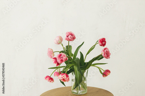 Stylish beautiful pink tulips bouquet in vase on wooden table in rustic room. Floral arrangement in farmhouse. Spring flowers composition, copy space. Happy mothers day and womens