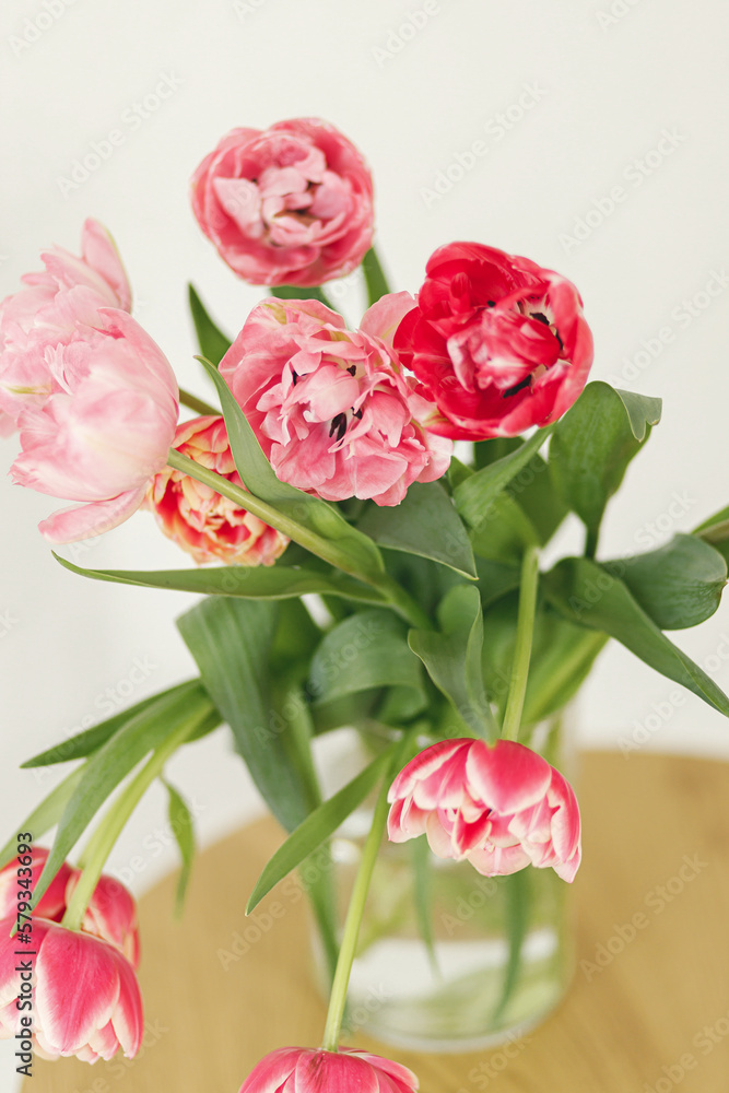 Stylish beautiful tulips bouquet in vase on wooden table in rustic room. Floral festive arrangement in farmhouse. Spring flowers composition. Happy mothers day and womens