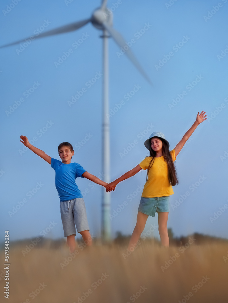 Boy and girl stand with raised hands. Wind turbine in the background. Future of kid and sustainable resources. People in the community with wind generators turbines Boy and girl stand with raised hands. Wind turbine in the background. Future of kid and sustainable resources. People in the community with wind generators turbines