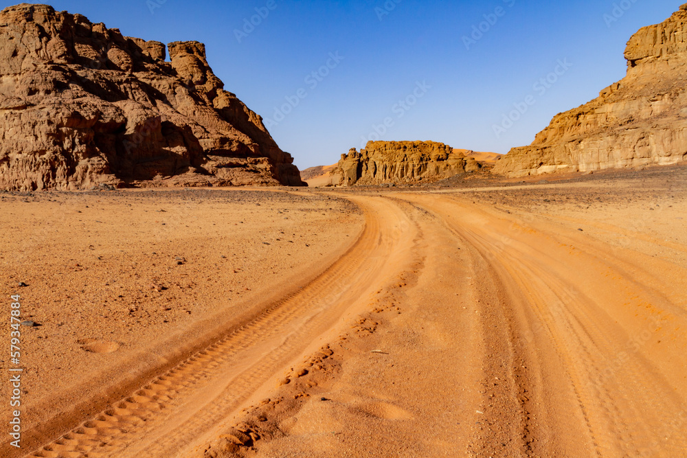 Empty sandy dirt road with tire tracks in Tassili National Park. Tadrart mountains, Acacus range. Tassili N'Ajjer National Park. Algeria, Africa Empty sandy dirt road with tire tracks in Tassili National Park. Tadrart mountains, Acacus range. Tassili N'Ajjer National Park. Algeria, Africa