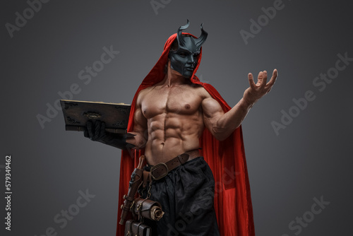 Portrait of evil fanatic with red cloak and mask against grey background.