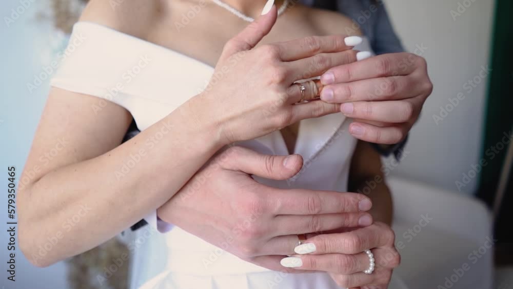 The groom in a suit and the bride in a beautiful dress with engagement rings on their hands are touching hands during a wedding stroll (close-up) The groom in a suit and the bride in a beautiful dress with engagement rings on their hands are touching hands during a wedding stroll (close-up)