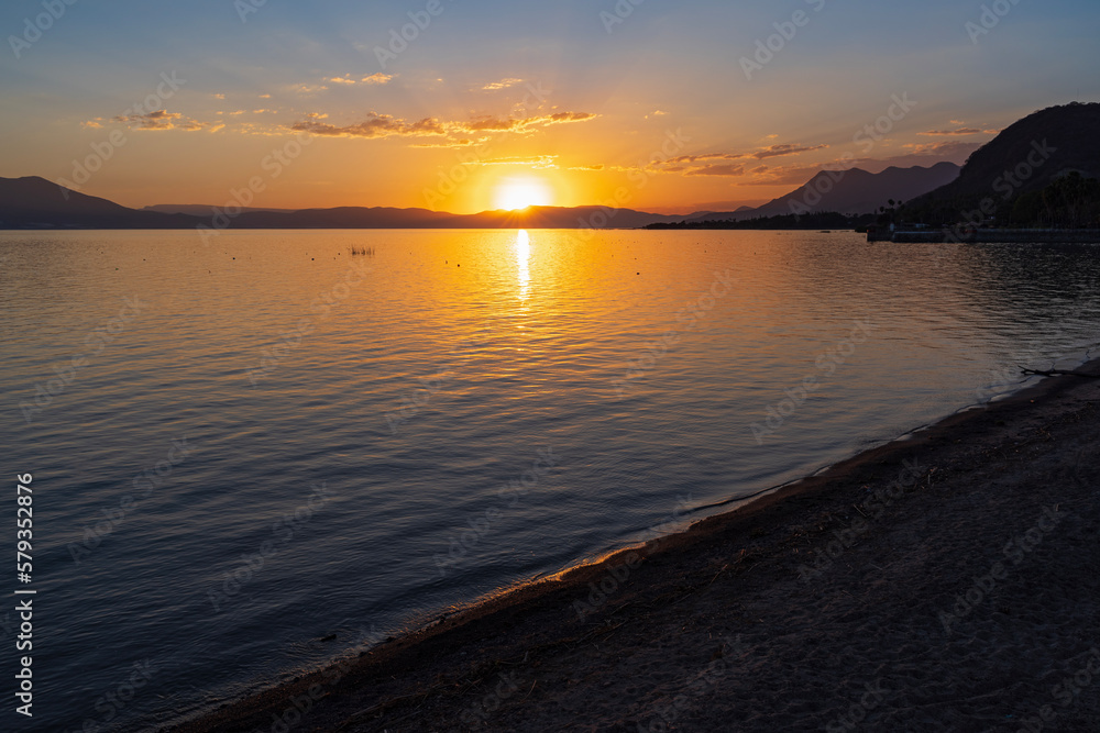 sun sets behind mountains surrounding lake chapala and illuminates water