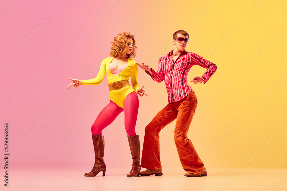 Young stylish emotional man and woman, professional dancers in retro style clothes dancing disco dance over pink-yellow background. 1970s, 1980s fashion, music concept - obrazy, fototapety, plakaty 