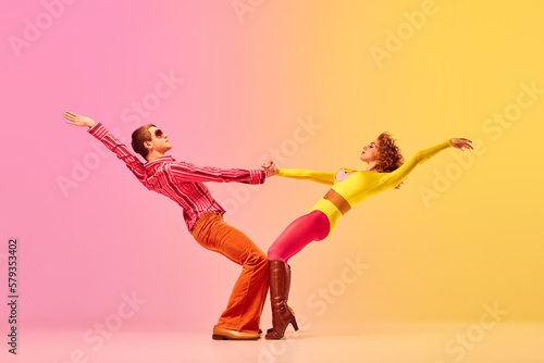 Fototapeta Young stylish emotional man and woman, professional dancers in retro style clothes dancing disco dance over pink-yellow background