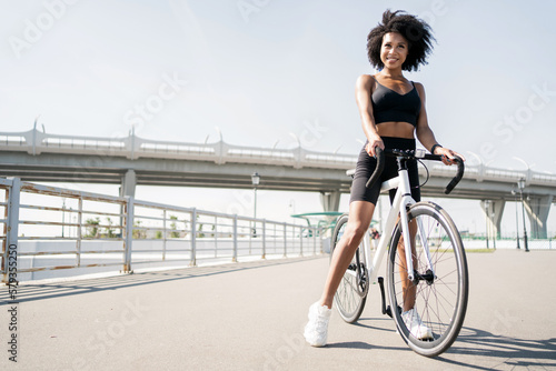 An active young woman in a tracksuit is a cyclist going for a walk outdoors on a white bicycle, eco transport in the city.