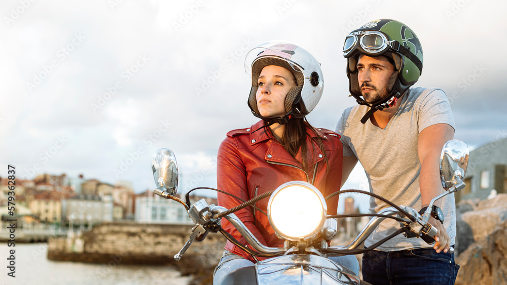 Biker couple wearing helmet riding touring motorcycle watching the sunset from the city. Couple of man and woman with helmet and copy space. Road safety and insurance concept