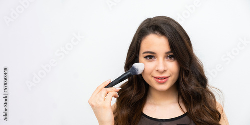 Joyful woman using makeup brush fro applying blusher on the banner with copy space