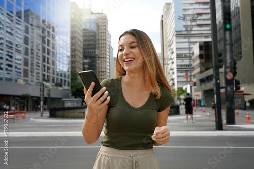 Young female entrepreneur watching her phone on Paulista Avenue in Sao Paulo finance district, Brazil photo