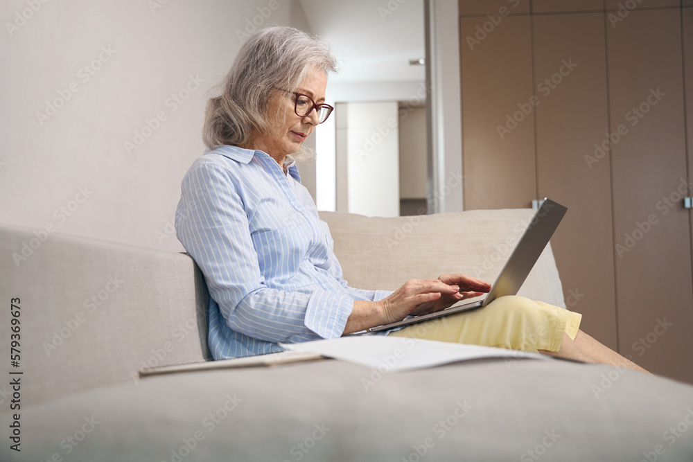 Cute grandmother works on a laptop at home on couch Cute grandmother works on a laptop at home on couch