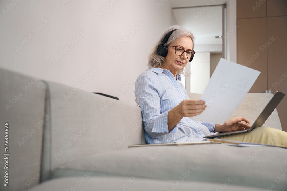 Concentrated gray-haired woman reads a summary at home on couch Concentrated gray-haired woman reads a summary at home on couch