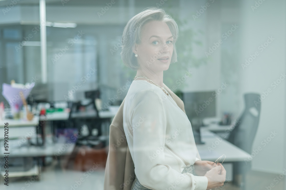 Portrait of a beautiful gray-haired caucasian woman in the office standing behind a glass wall. Portrait of a beautiful gray-haired caucasian woman in the office standing behind a glass wall.