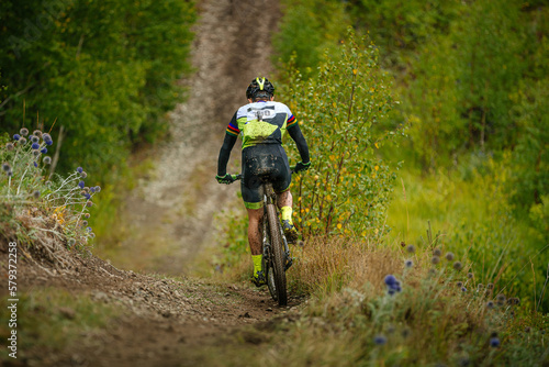 back male athlete on mountain bike ride forest trail. dirt on feet and body. cross-country cycling competition