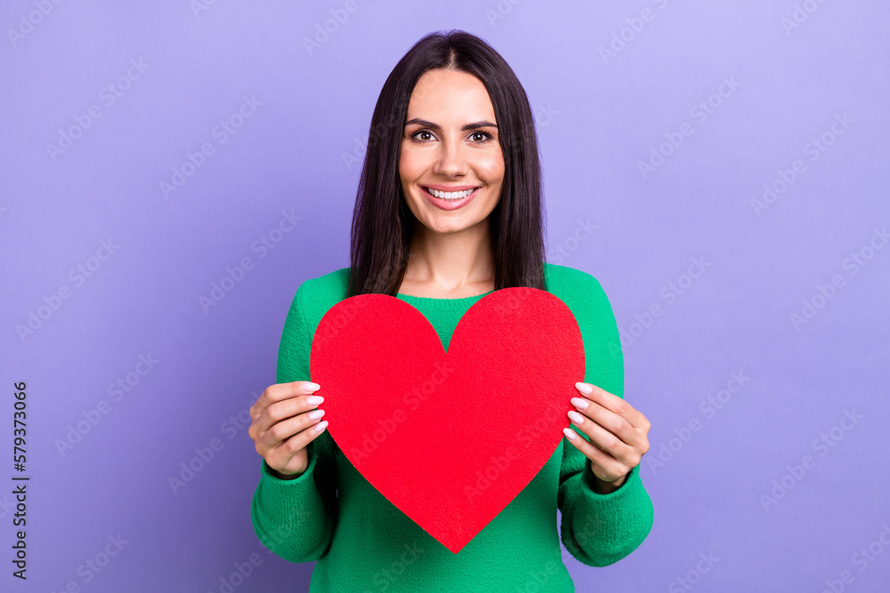Photo of shiny charming woman wear green pullover holding arms red heart isolated purple color background Photo of shiny charming woman wear green pullover holding arms red heart isolated purple color background